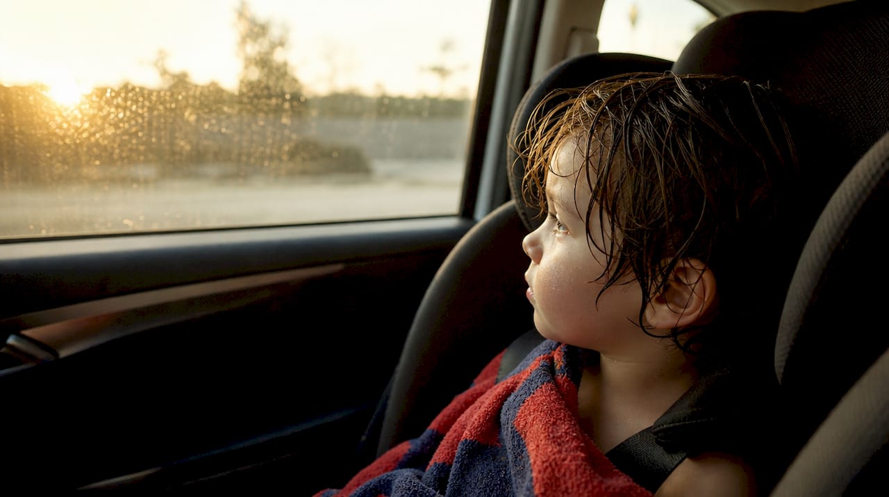 Child with wet hair drying in car seat after swim