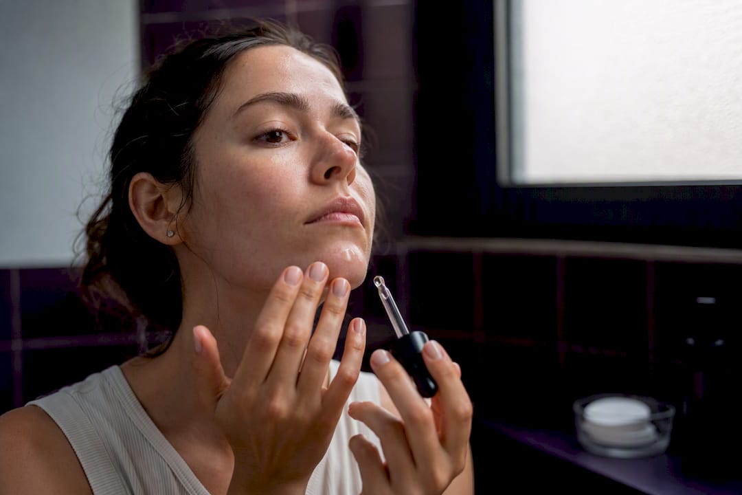 Hands applying serum to nose and chin