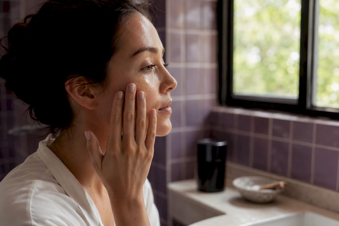 Hands applying serum to cheek
