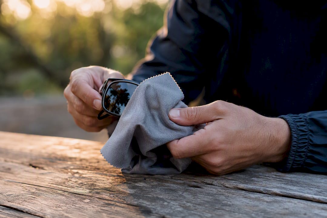 Hands wiping sunglasses lenses with microfiber cloth