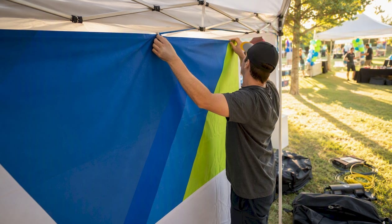 Hands attaching tent backdrop panel outdoors