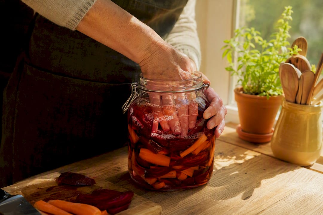 Hands pressing vegetables in fermentation jar