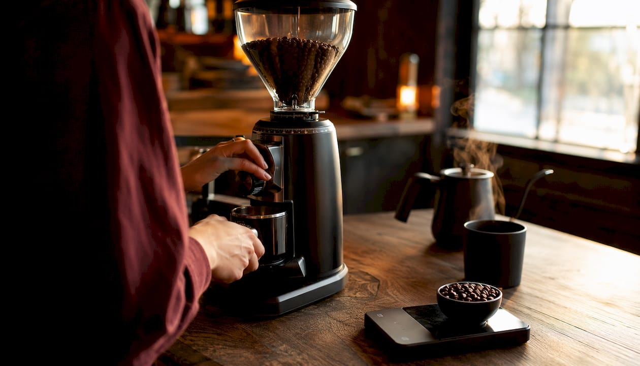 Hands adjusting burr grinder with scale nearby