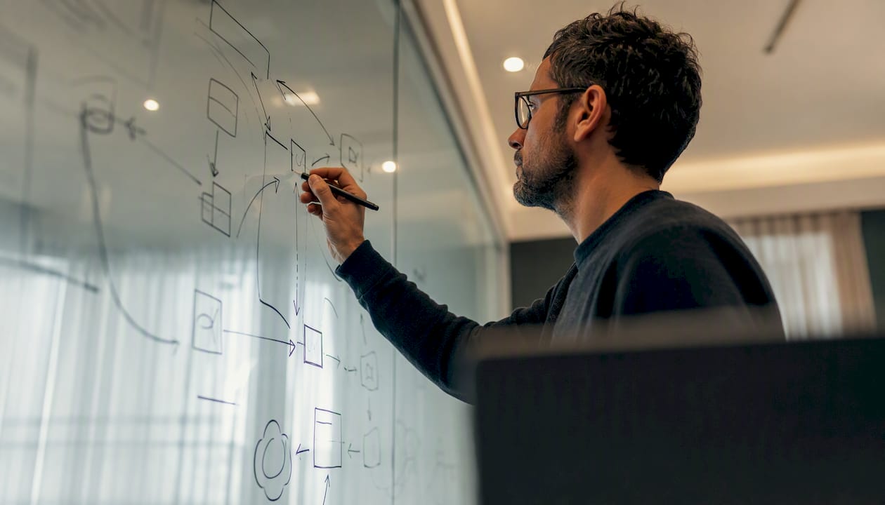 Hands mapping data flows on glass board