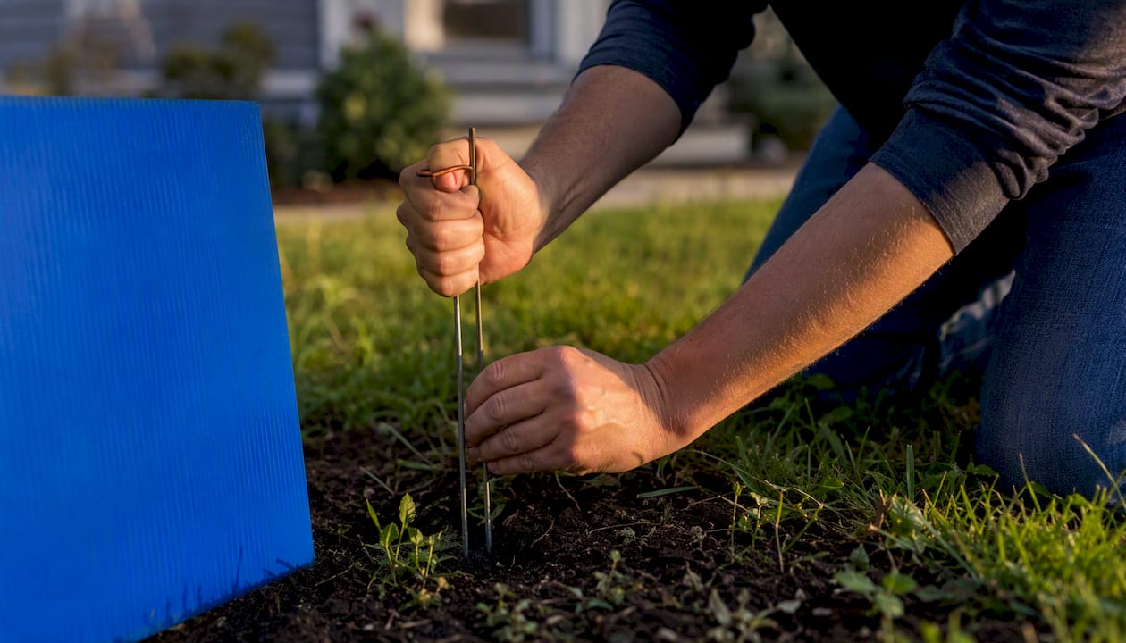 Hands installing wire H-stake in lawn soil