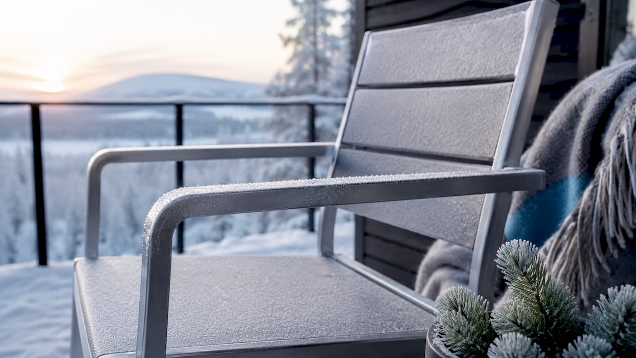 En frostig stol i aluminium står ute på altanen av trä.
