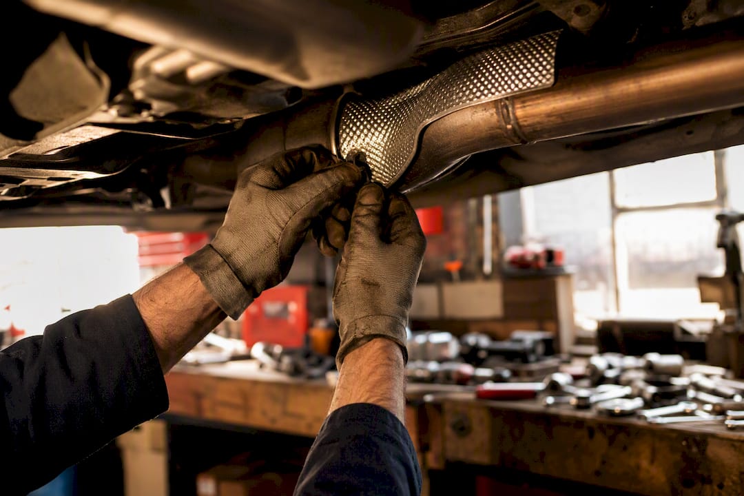 Hands tightening loose heat shield on exhaust pipe