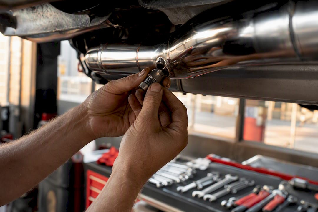 Technician installing O2 sensor spacer on exhaust pipe