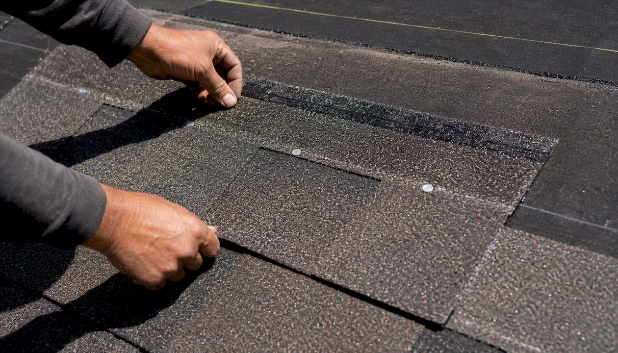 Close-up of wind-rated shingles being installed with nails and seal strip