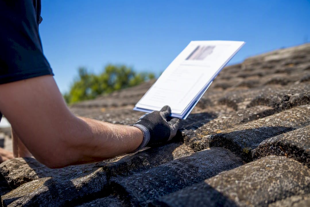 Gloved hand holding roof inspection report over roof tiles