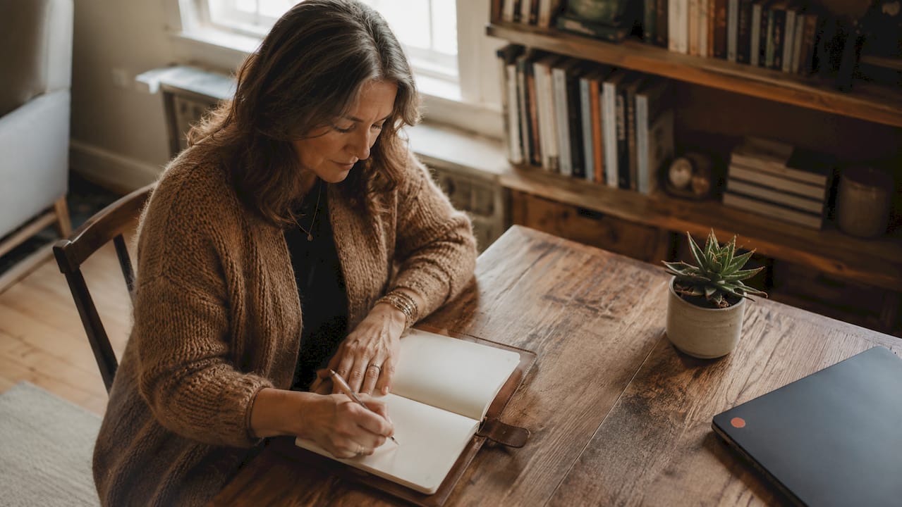 Woman journaling at home desk in afternoon light