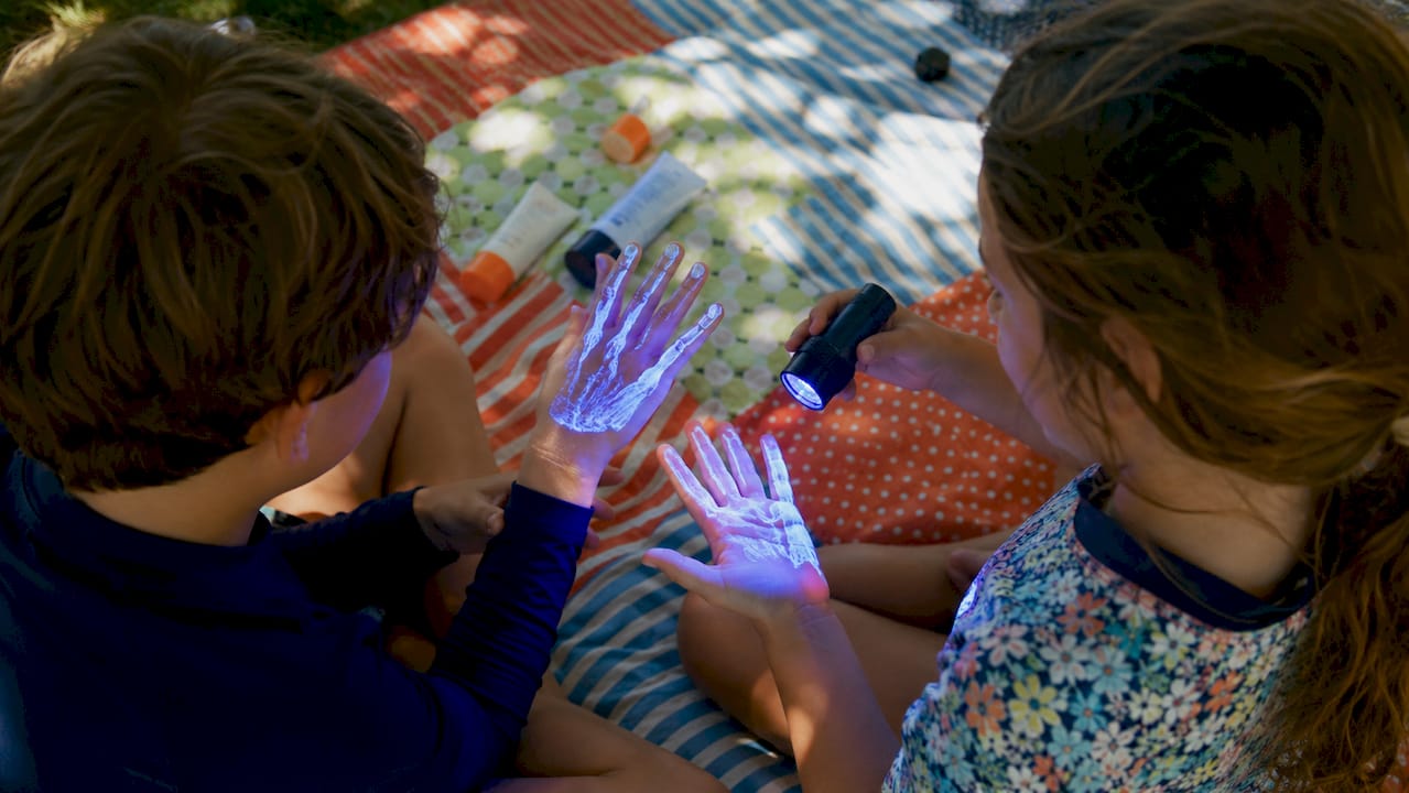 Children’s hands glowing under blacklight sunscreen