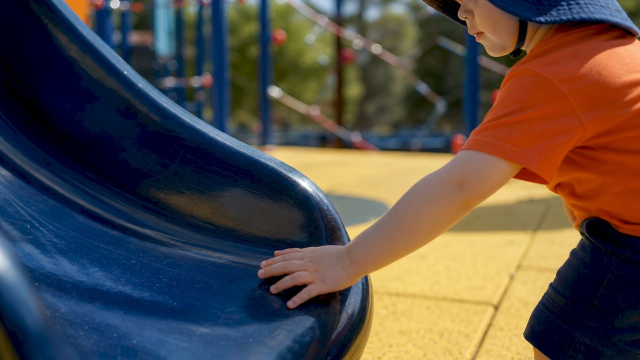 Child's hand touching hot playground metal surface
