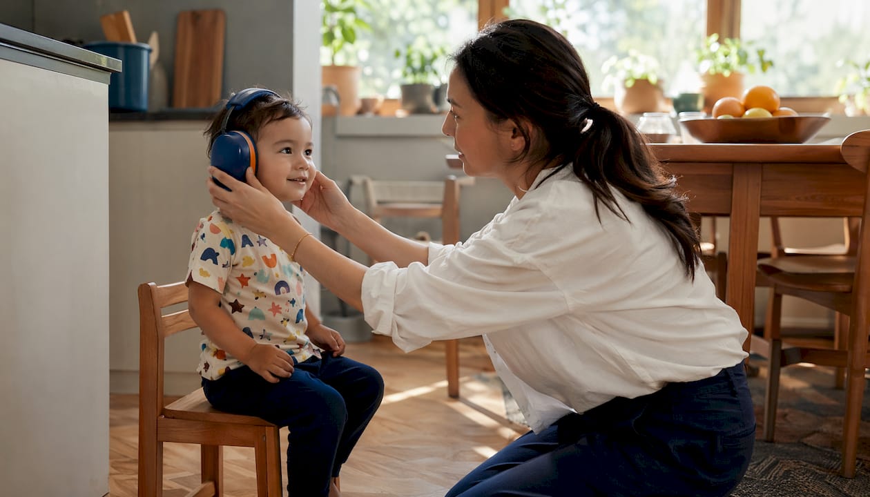 Parent fitting over-ear earmuffs on toddler indoors