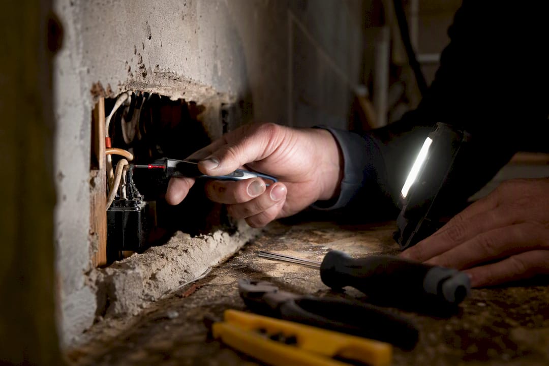 Hand testing electrical wiring inside wall