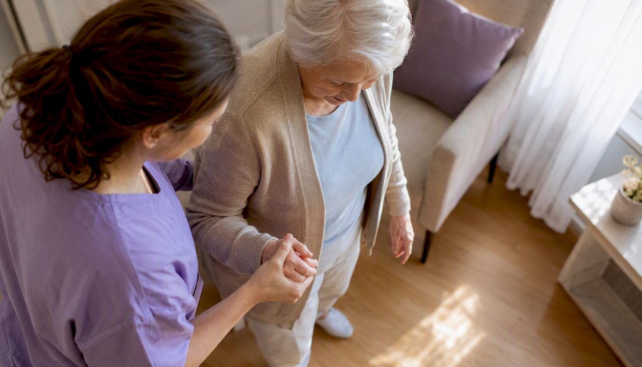 Caregiver supporting elderly woman's arm in kitchen