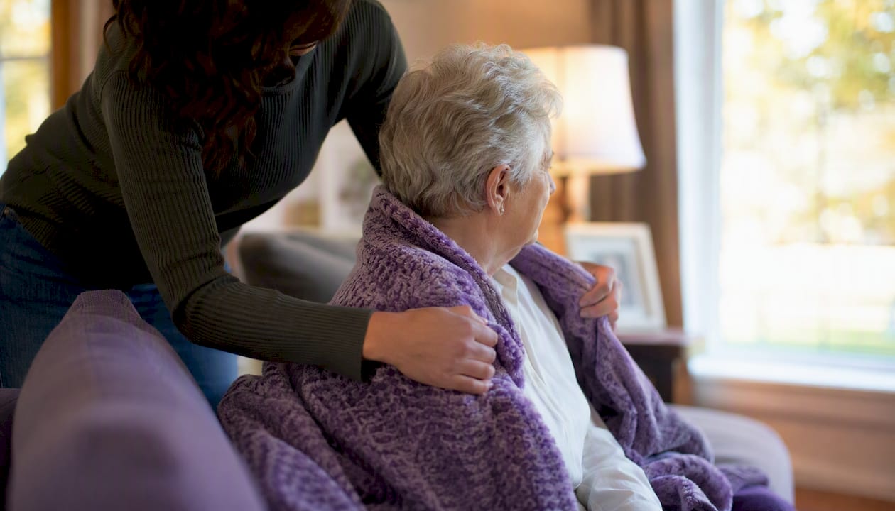 Caregiver placing blanket on elderly adult
