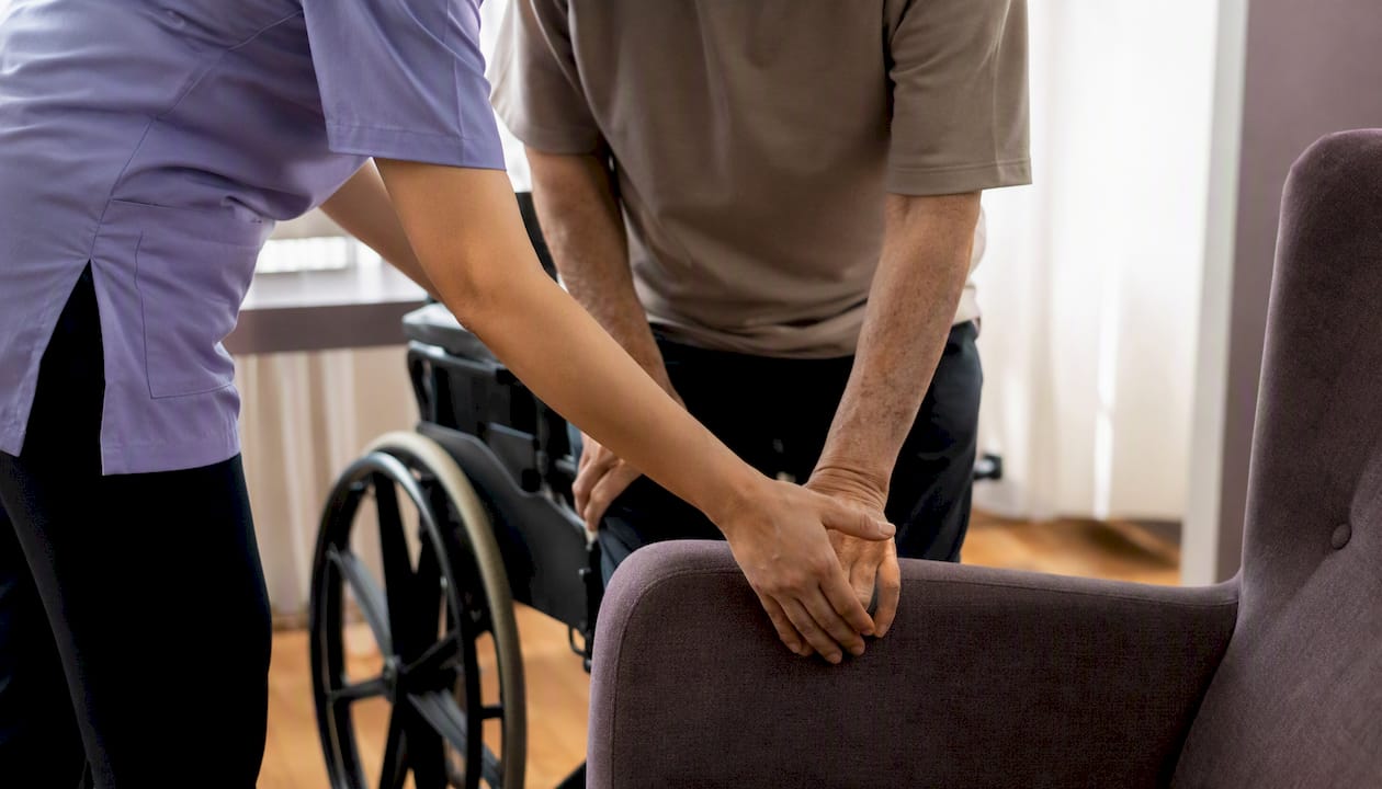 Caregiver assisting elderly with bed transfer