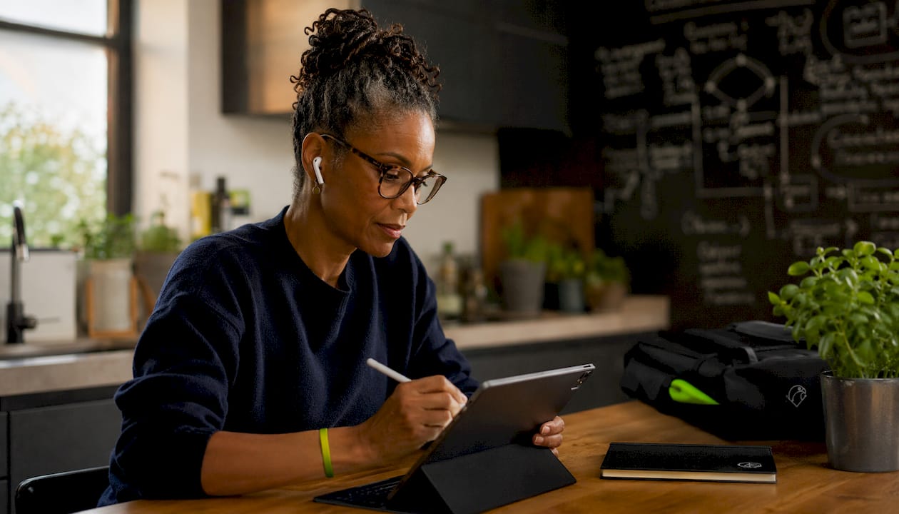 Coach working on tablet with earbuds in home office