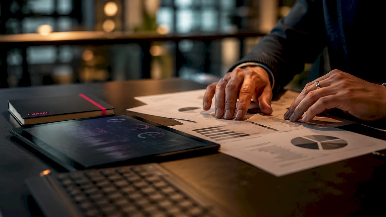 Dettaglio ravvicinato di una postazione di lavoro professionale, con dispositivi dal design scuro e documenti ordinati sulla scrivania.