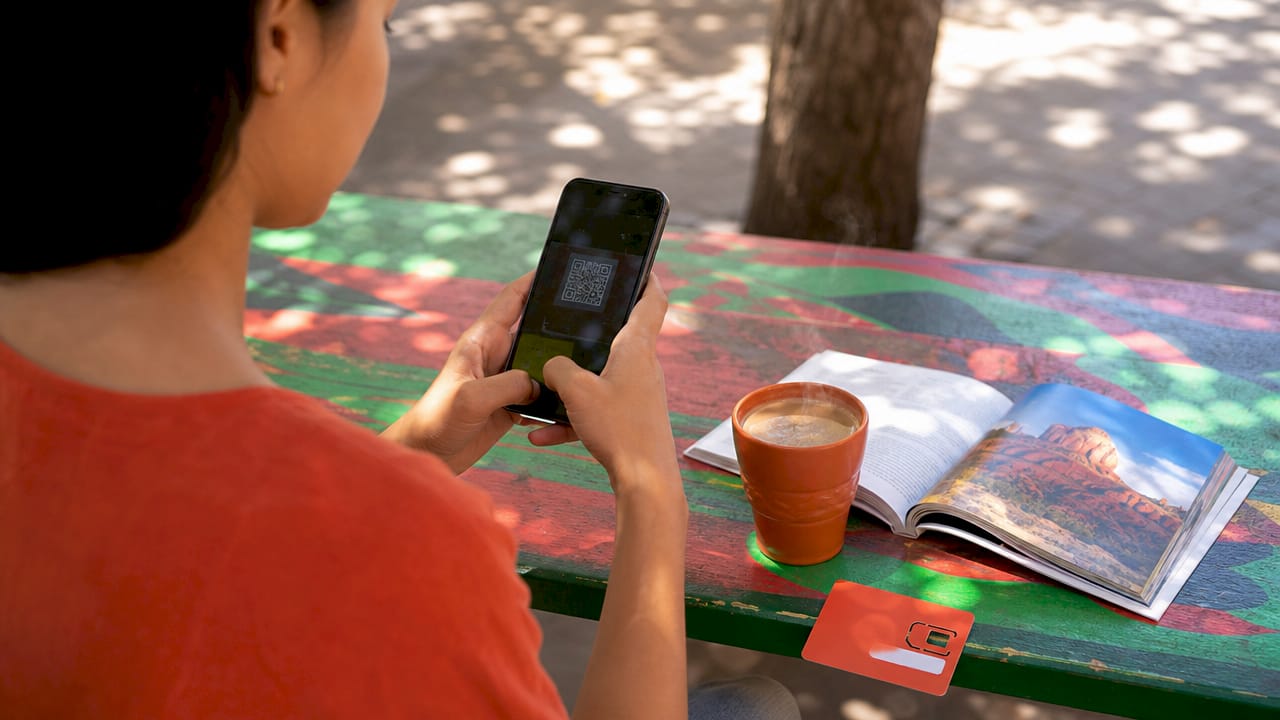 Hands activating eSIM on smartphone in café
