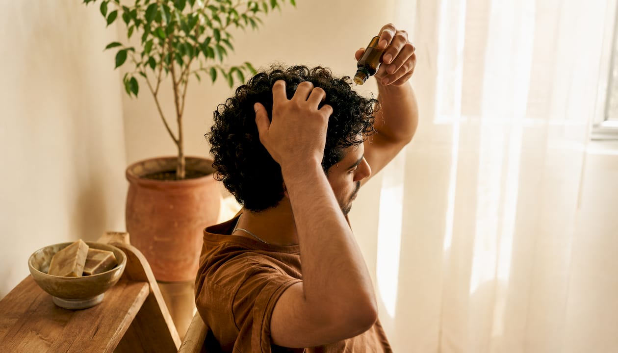 Young man massaging scalp with seed oil drops
