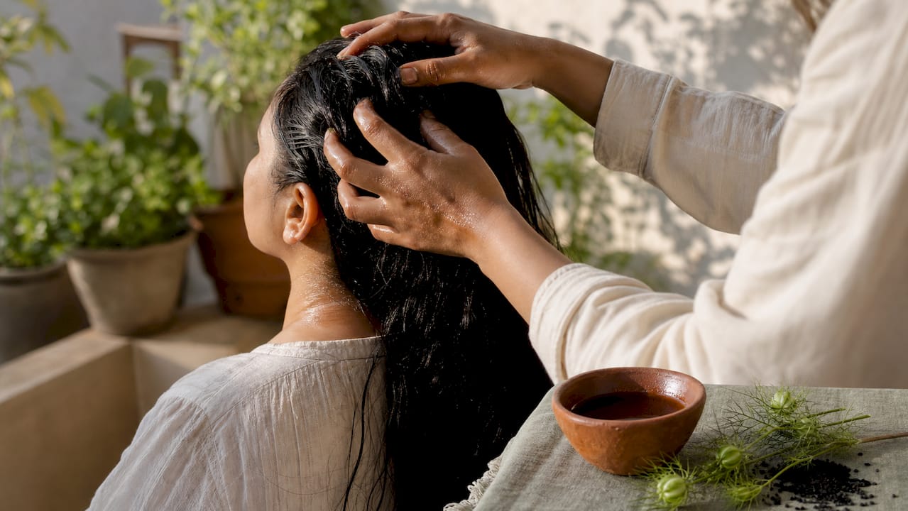 Hands massaging black seed oil into scalp