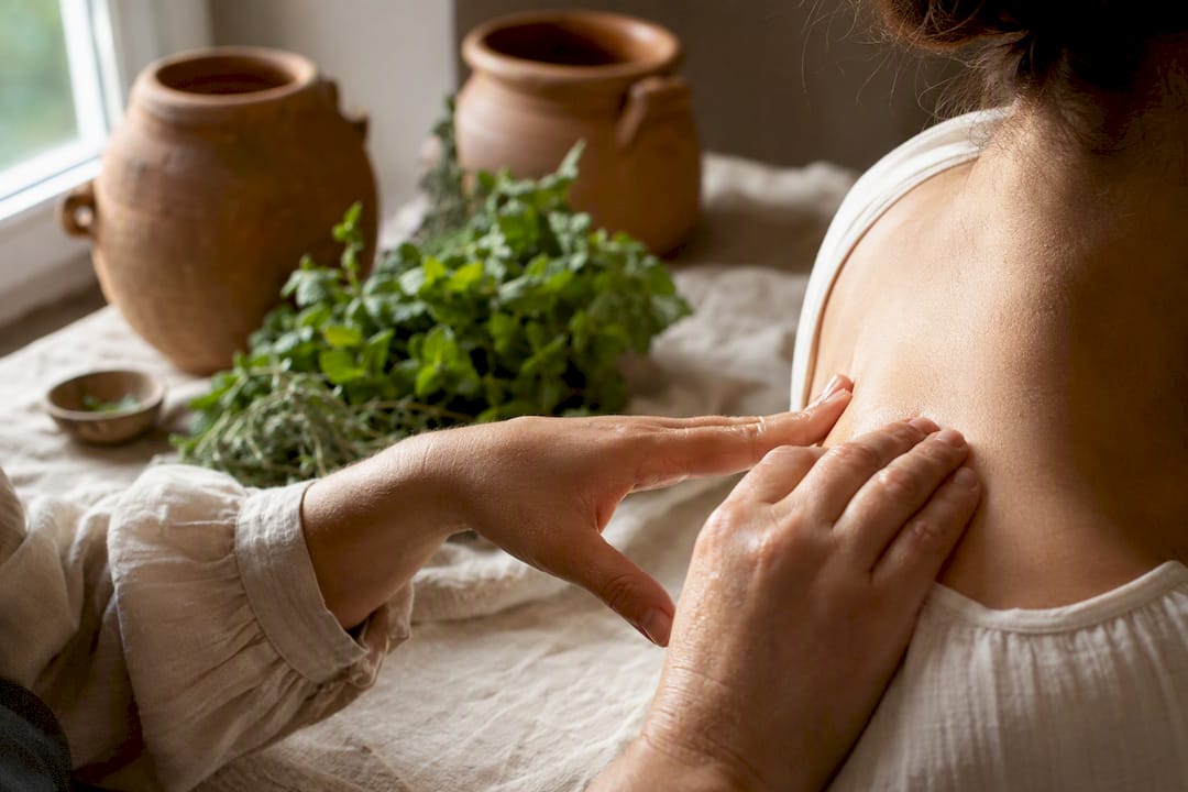 Hands applying essential oil with fresh botanicals nearby