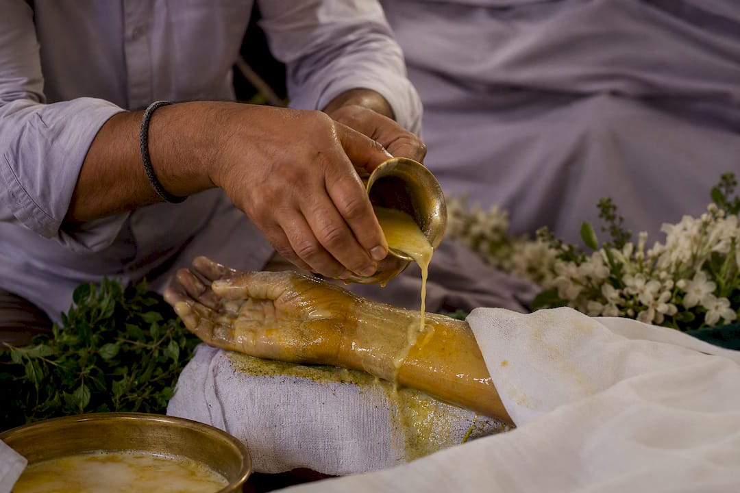 Hands washing deceased with turmeric milk and tulsi leaves