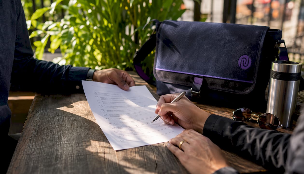 Hands exchanging signing verification documents on table.