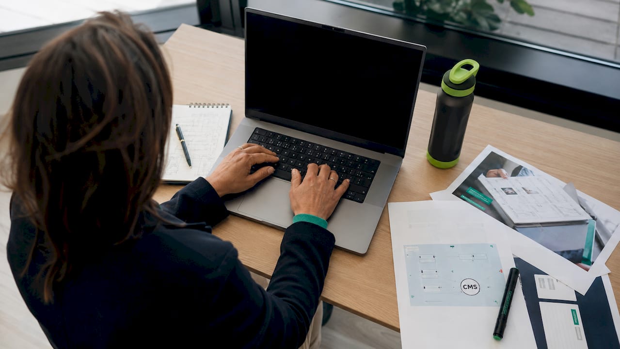 Des mains en train de taper sur un clavier, avec des outils CMS posés juste à côté.