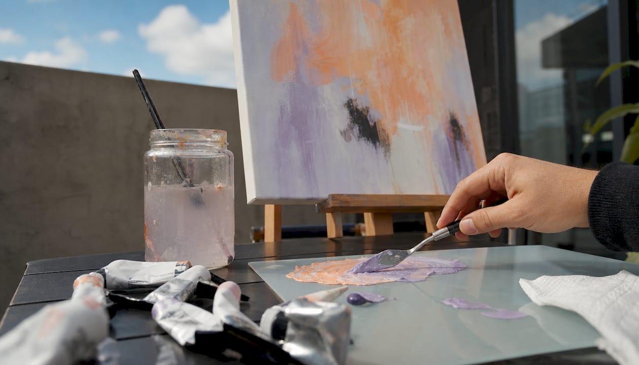 Artist mixing paint beside calming landscape canvas art