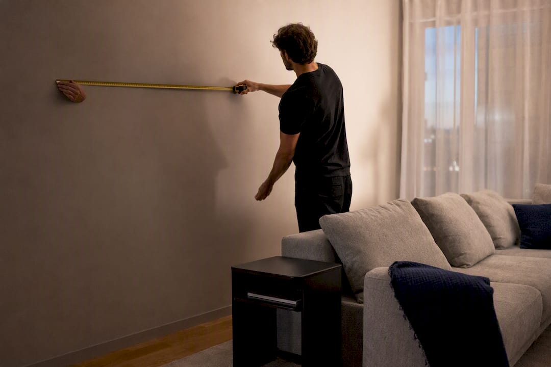 Hands measuring empty wall space with tape