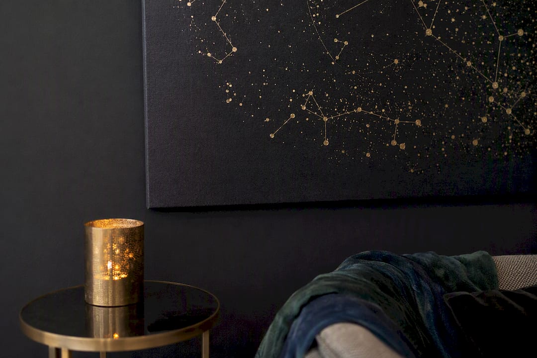Gold constellation art on black wall with warm lighting