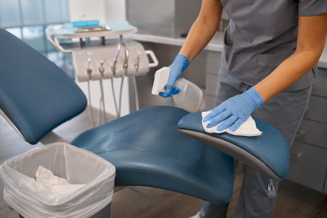 Gloved hands disinfecting medical exam table