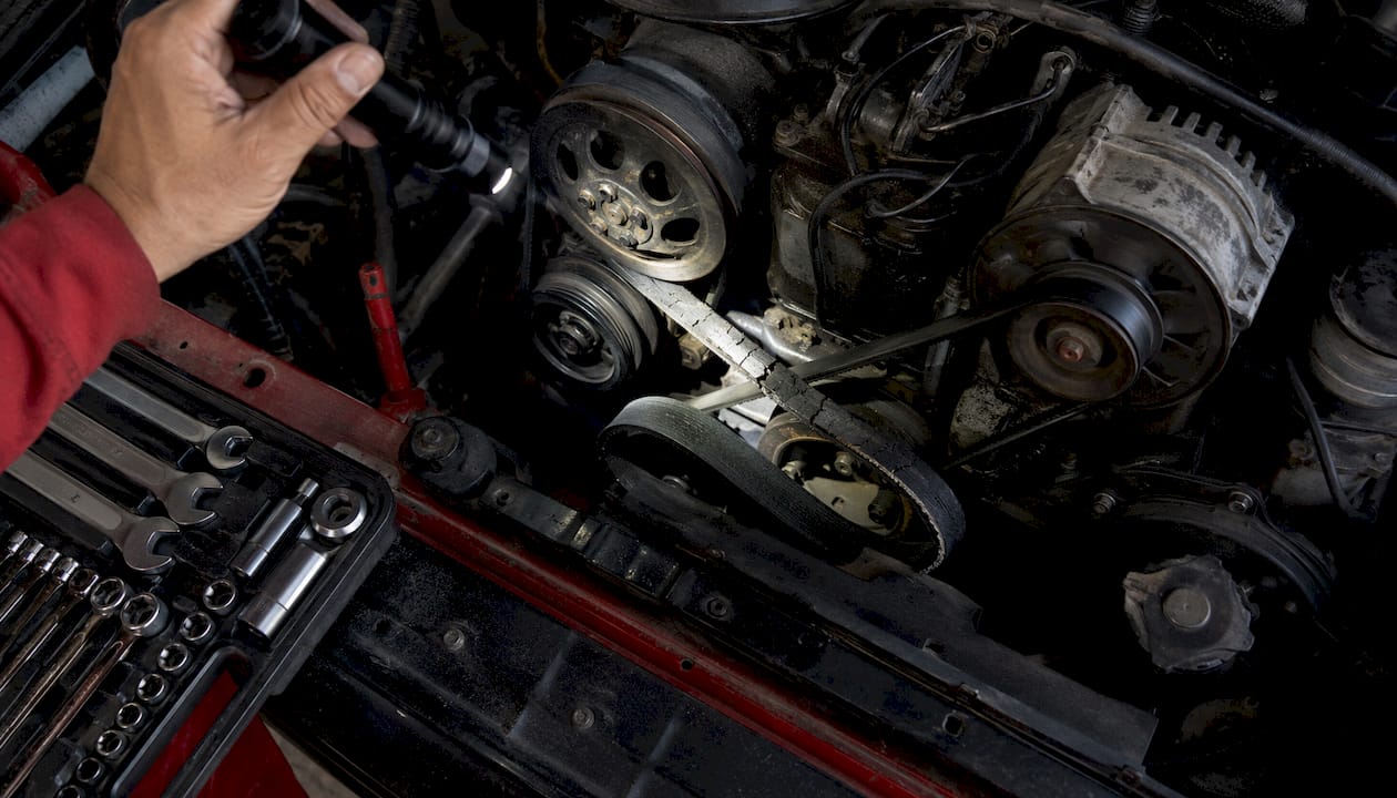 Mechanic inspecting cracked serpentine belt with flashlight