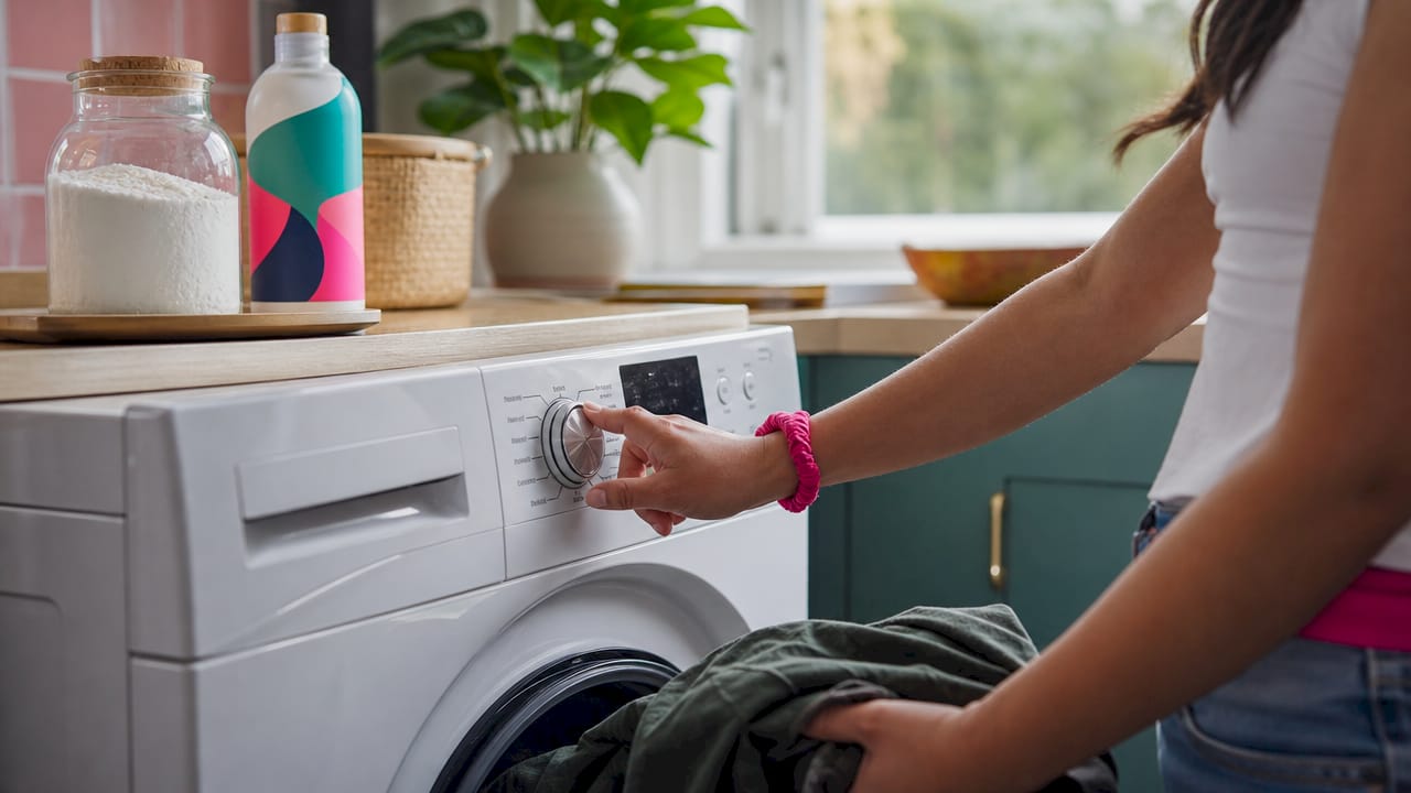 Hands setting washing machine to cold cycle