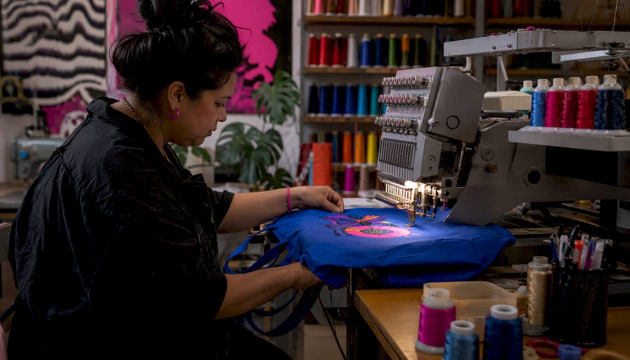 Hands guiding embroidery machine on canvas tote bag