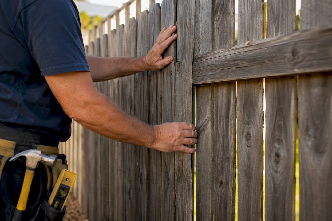 Hands inspecting wooden fence section outdoors