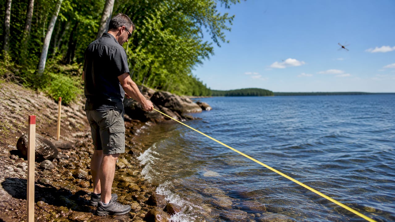Surveyor measuring lake shoreline frontage at dawn