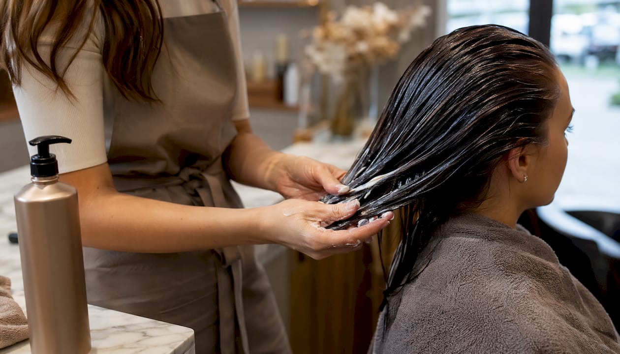 Hands applying conditioner to wet hair strands