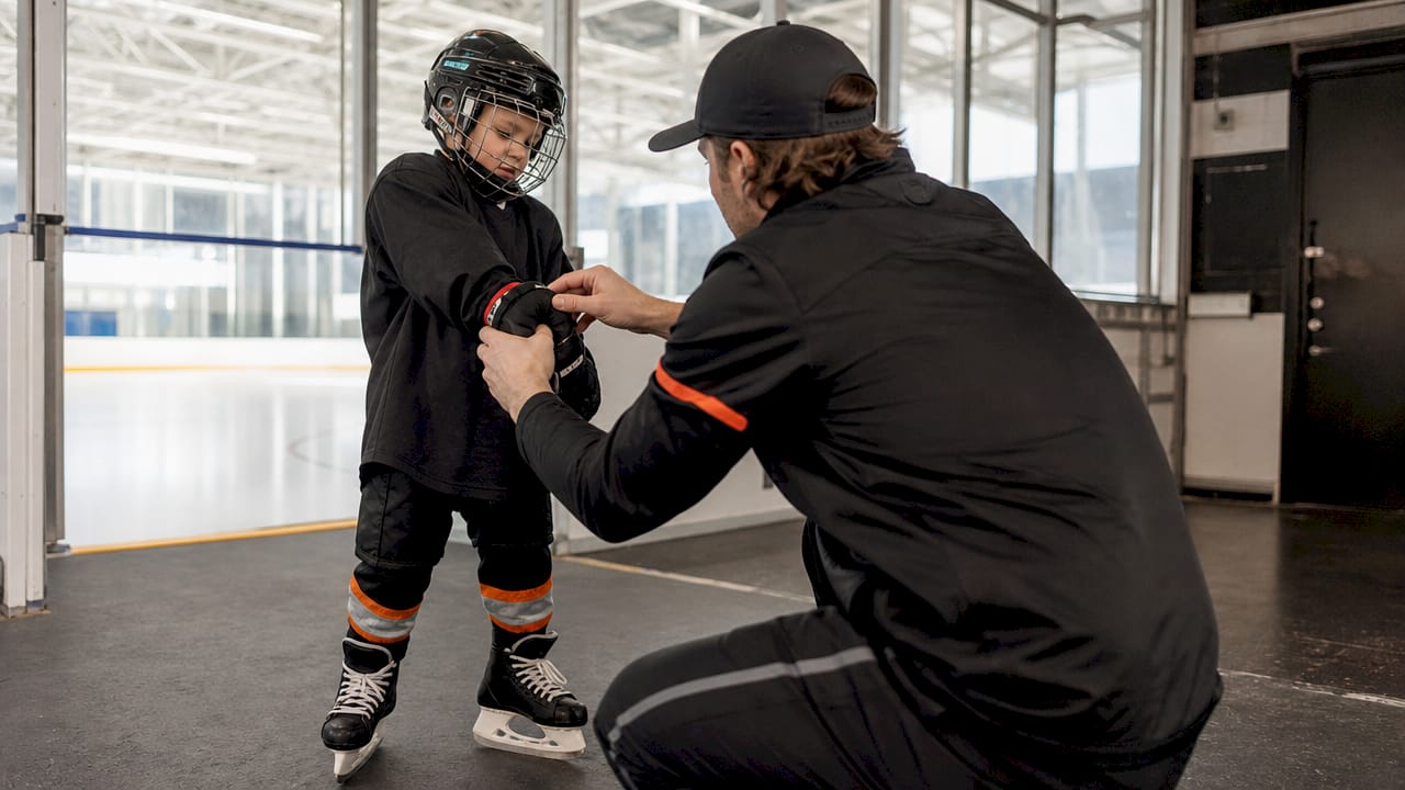 Close-up of youth hockey player fitting gloves near rink