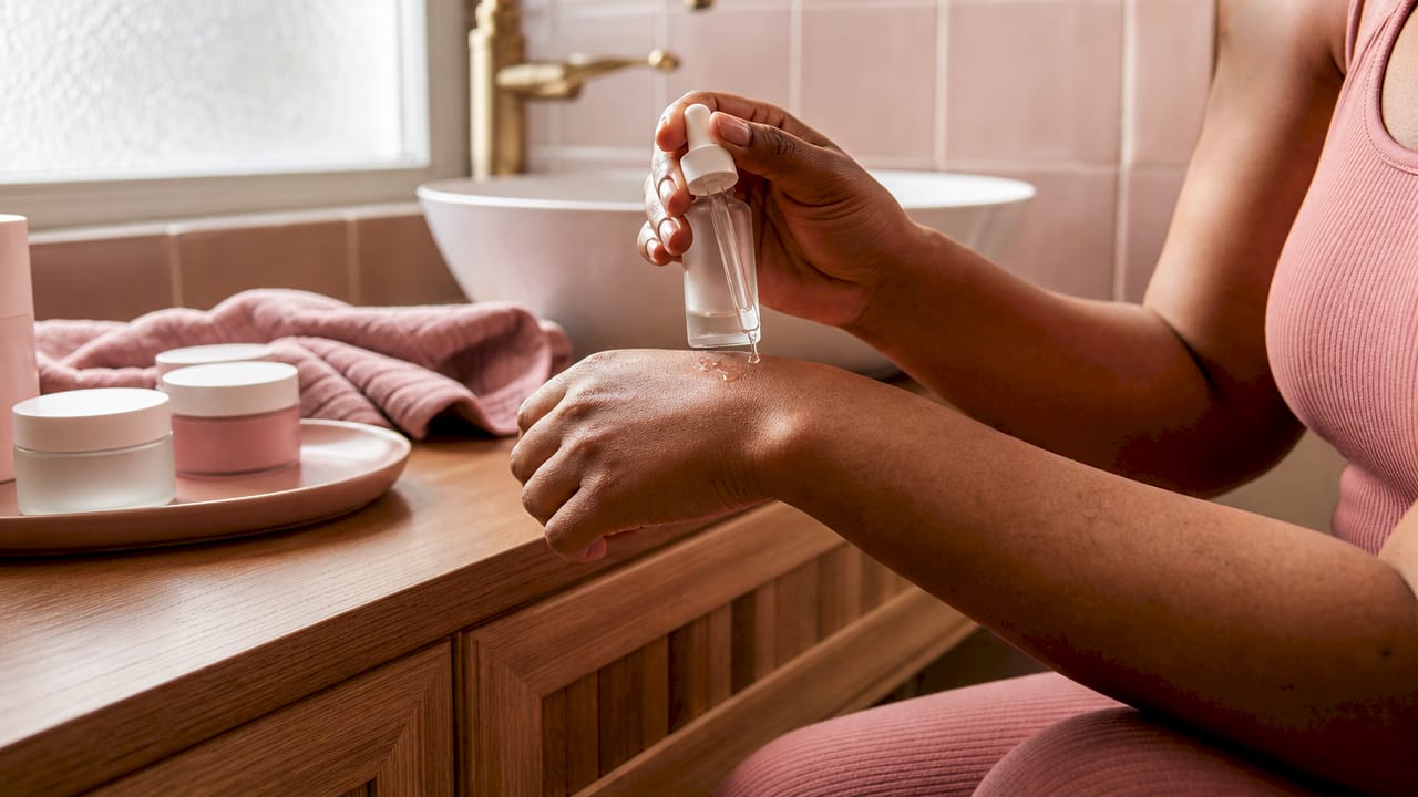 Hands holding serum bottle applying skincare