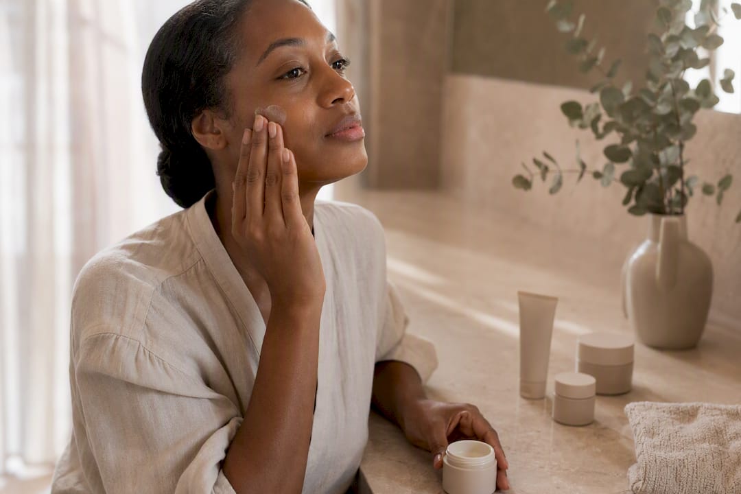 Hand applying tinted mineral sunscreen on dark skin