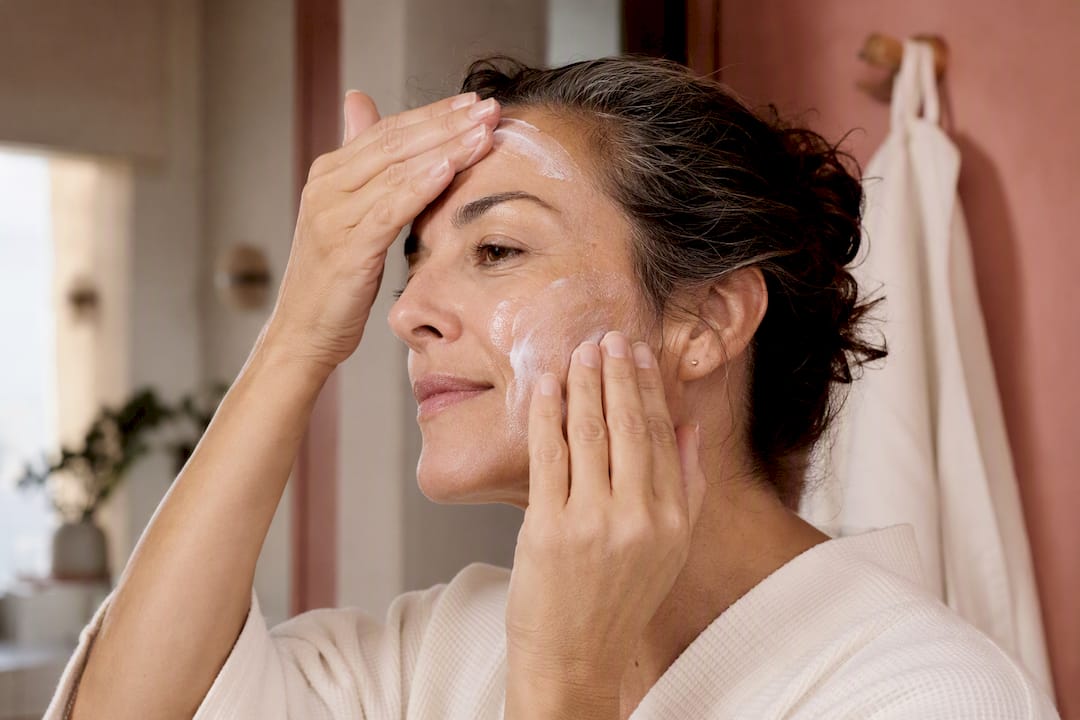 Woman applying sunscreen to face in bathroom