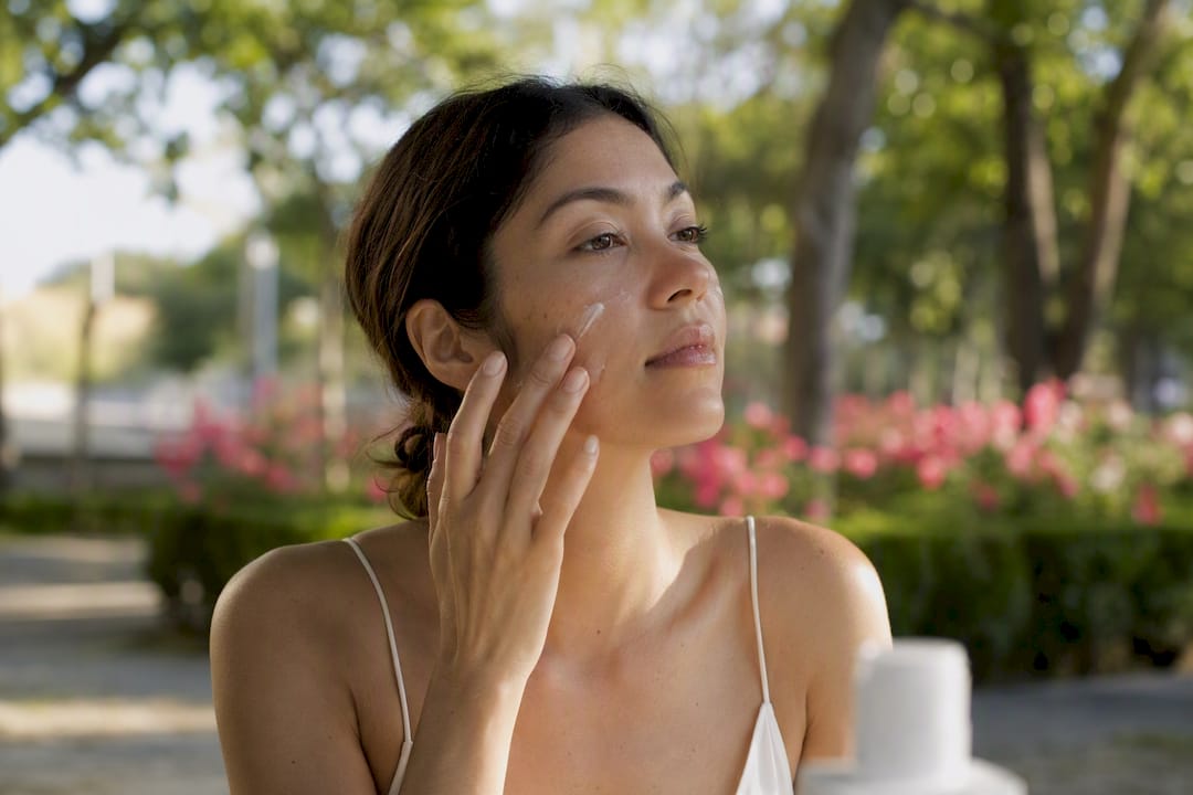 Woman applying facial sunscreen outdoors close-up