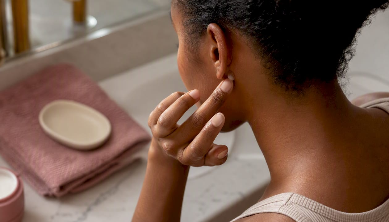 Woman applying skincare patch test behind ear