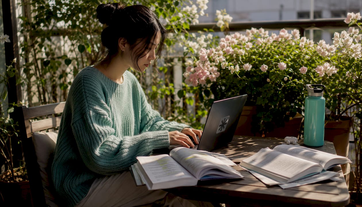 Hands typing on laptop among study materials