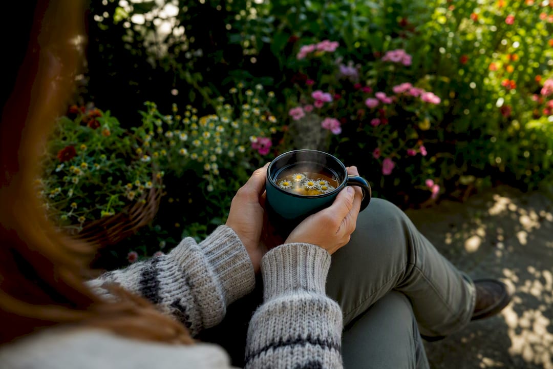 Person holding tea mug on park bench resting