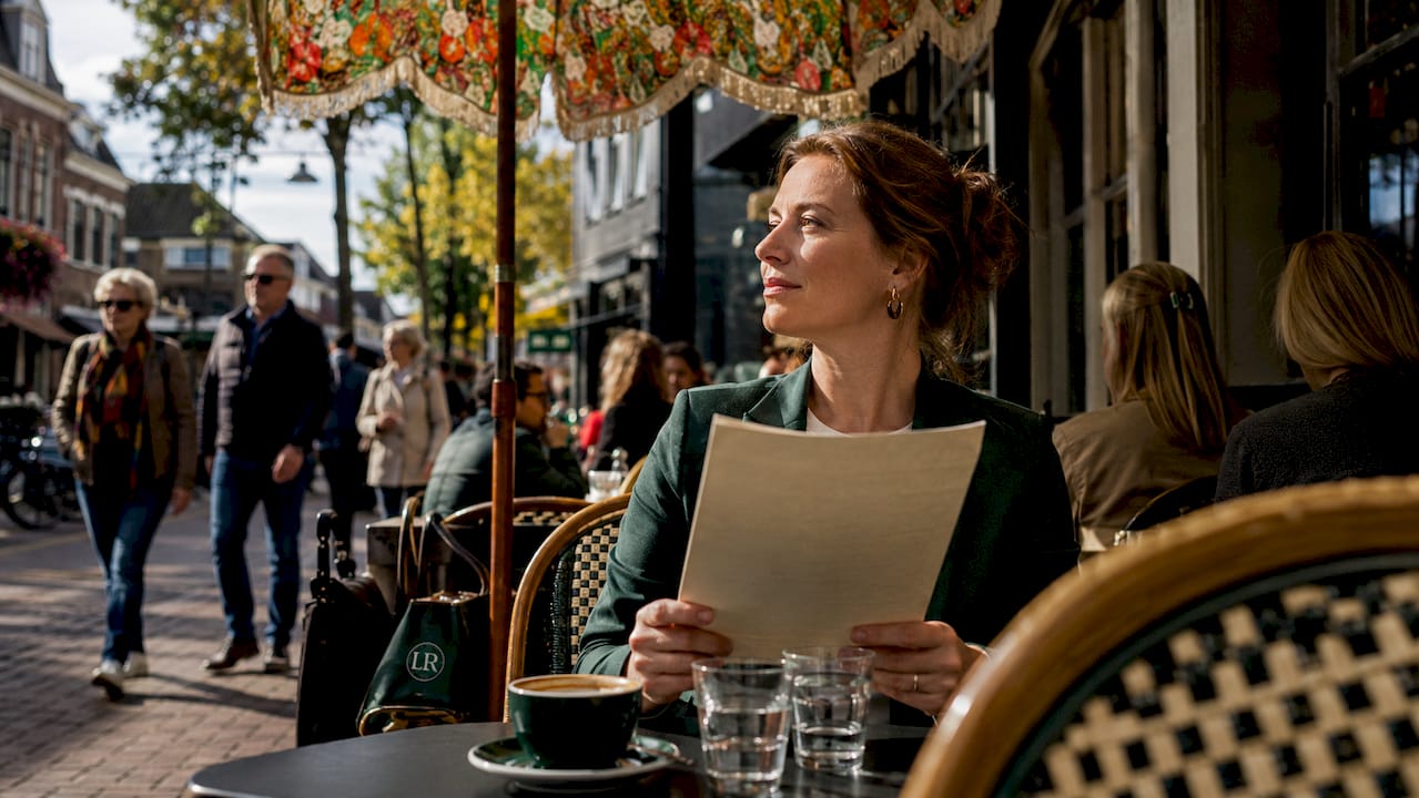 Een vrouw staat bij de openstaande deur van een brasserie en bekijkt de menukaart.